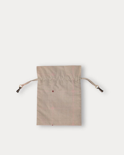 A small beige fabric drawstring pouch with a subtle pink grid pattern and a tiny red embroidered detail, shown on a light gray background.