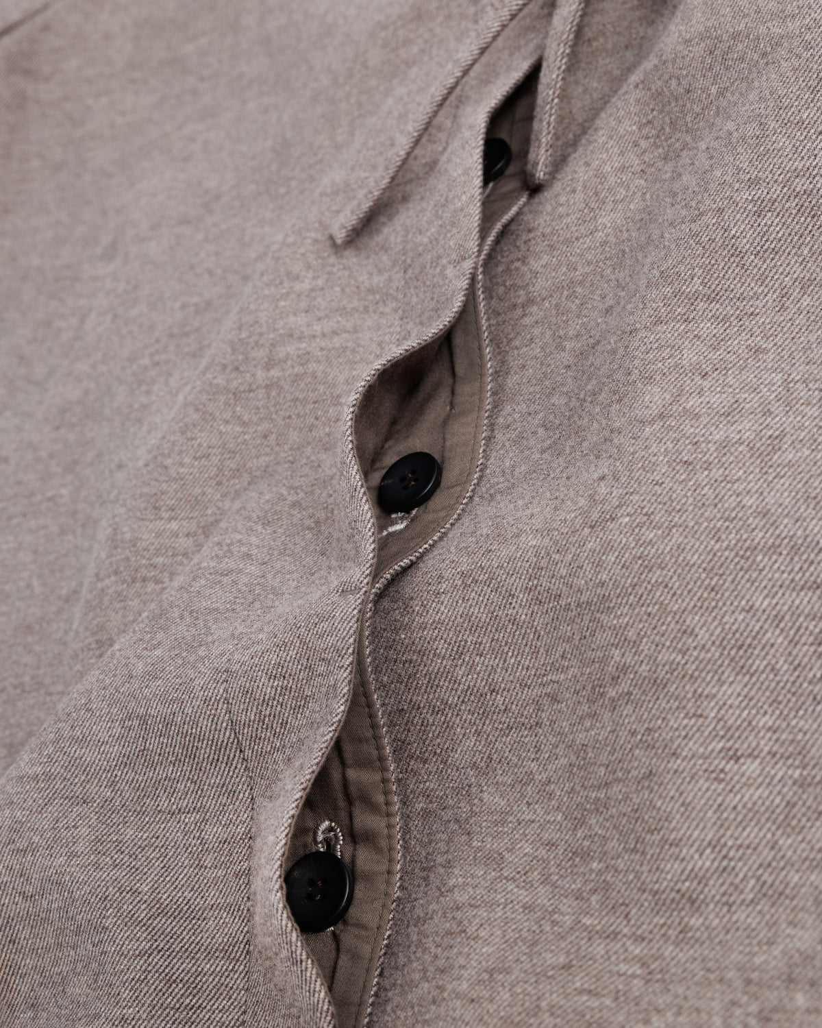 Close-up of a taupe-brown fabric with buttons and ruffled details