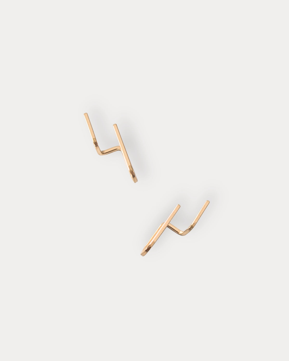 A pair of minimalist 14KGF gold-toned geometric stud earrings with a double-prong design, displayed on a clean, light gray background.