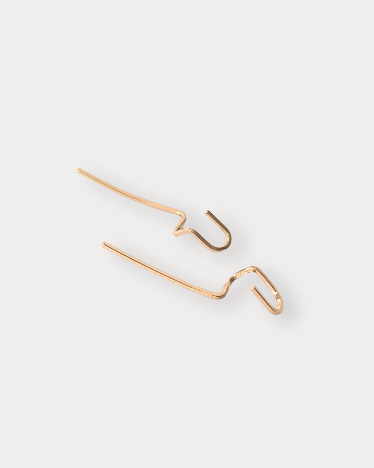 A pair of minimalist 14KGF gold-toned wire earrings with a wavy, abstract design, displayed on a clean, light off-white background.