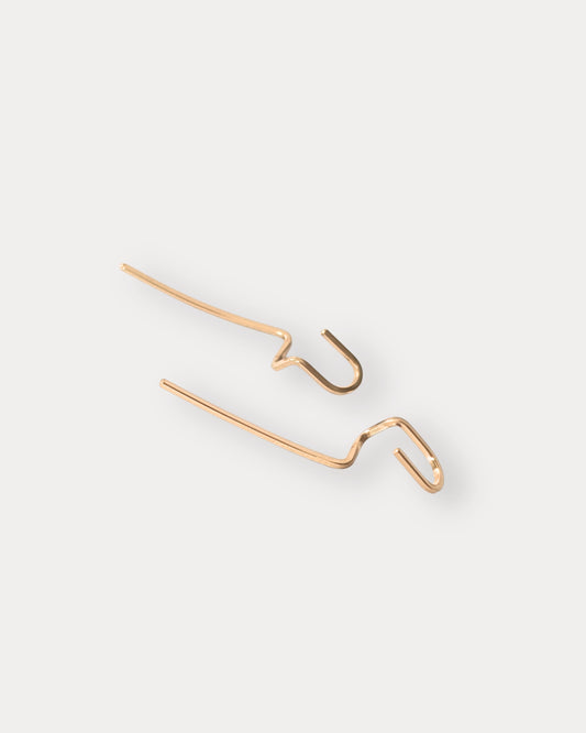 A pair of minimalist 14KGF gold-toned wire earrings with a wavy, abstract design, displayed on a clean, light off-white background.