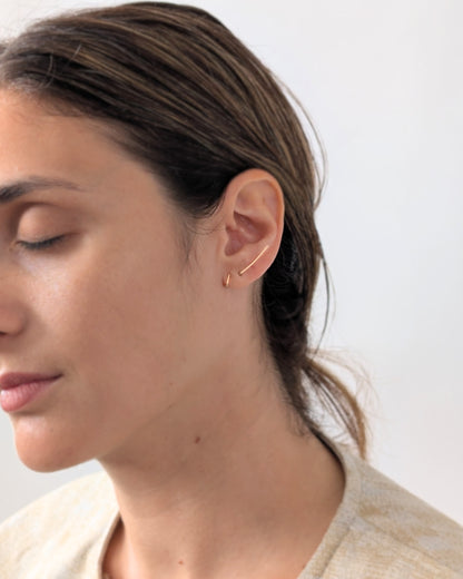 A close-up side profile of a woman wearing a delicate 14KGF gold earring against a plain light background.