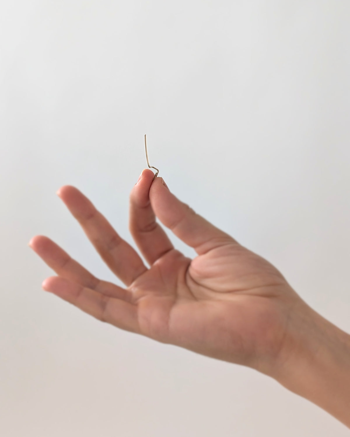 A hand holding a very thin 14KGF gold-toned earring against a plain light background.