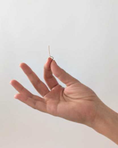 A hand holding a very thin 14KGF gold-toned earring against a plain light background.
