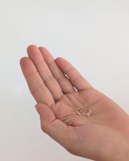 A close-up of a person's open palm holding a pair of tiny 14KGF gold-toned geometric stud earrings against a plain light background.