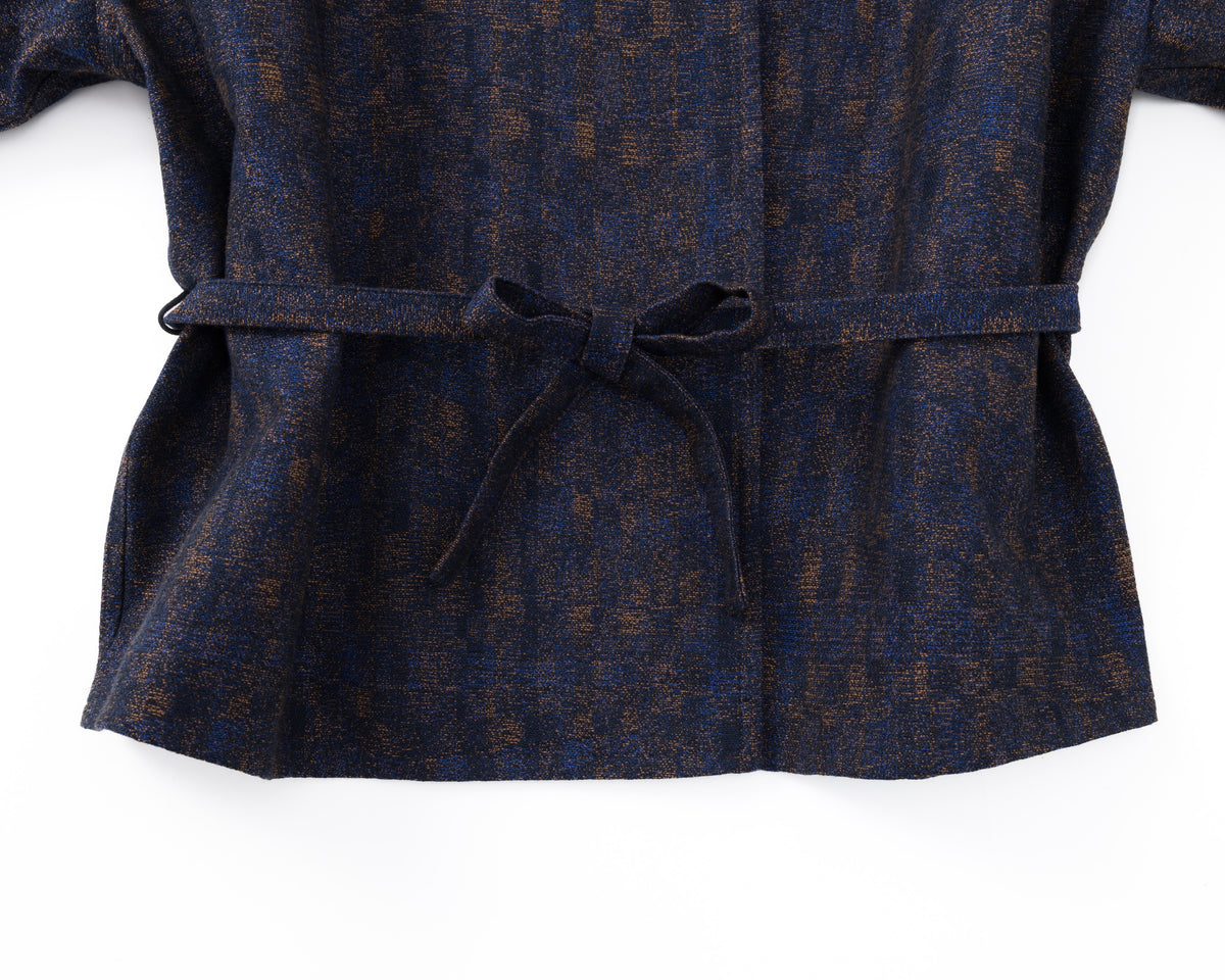 Detail of the waist of a navy shirt-jacket with a subtle pattern and a drawstring on a white background