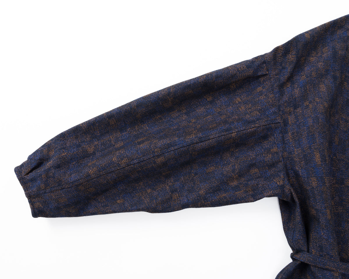 Detail of the sleeve of a navy shirt-jacket with a subtle pattern on a white background