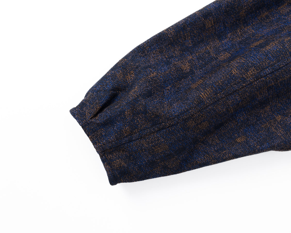 Detail of the sleeve of a navy shirt-jacket with a subtle pattern on a white background