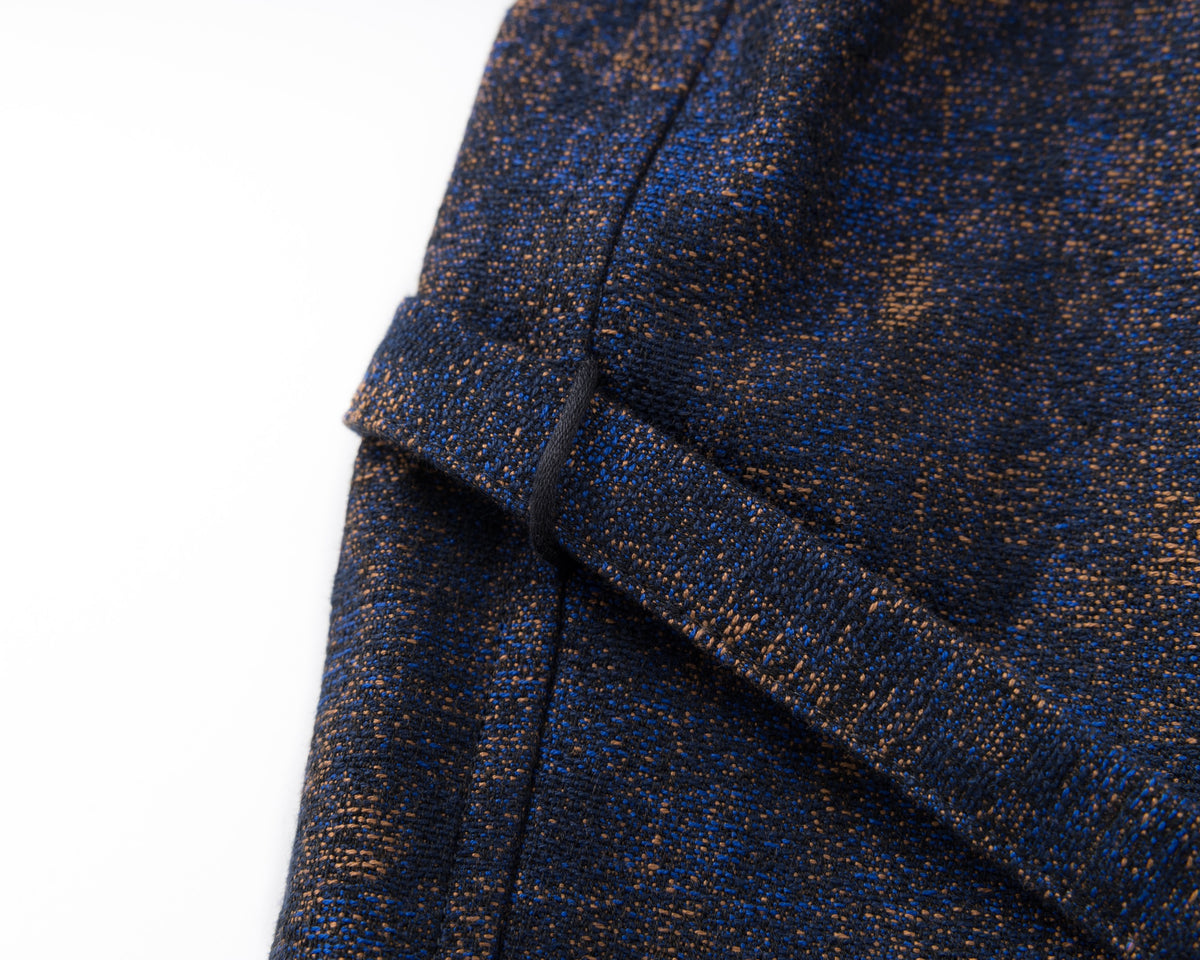 Detail of the waist and drawstring of a navy shirt-jacket with a subtle pattern on a white background