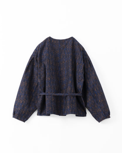 The back side of a dark navy blue cropped jacket with a subtle brown and gold abstract pattern, featuring balloon sleeves and a matching waist tie belt, shown against a light grey background.