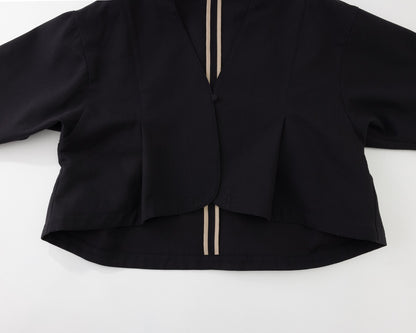 A black long-sleeve cropped cardigan or jacket with a V-neckline, featuring two vertical beige stripes down the front center and a button closure at the collar, laid flat on a white background.