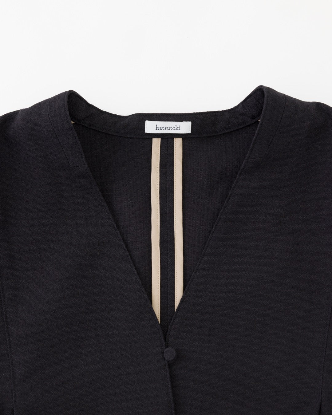 Close-up of a black V-neck top with two vertical beige stripes down the center front and a visible brand label at the collar reading harajuku.