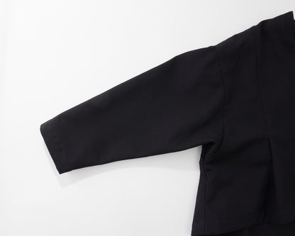 A close-up of a black long-sleeve garment laid flat on a white background, showing the sleeve, shoulder seam, and side drape.