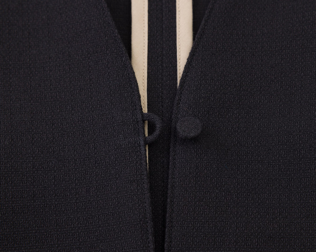 Close-up of a dark navy textured knit garment with a cream-colored center stripe and matching dark buttons.