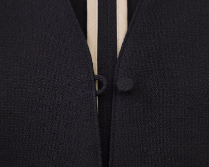 Close-up of a dark navy textured knit garment with a cream-colored center stripe and matching dark buttons.