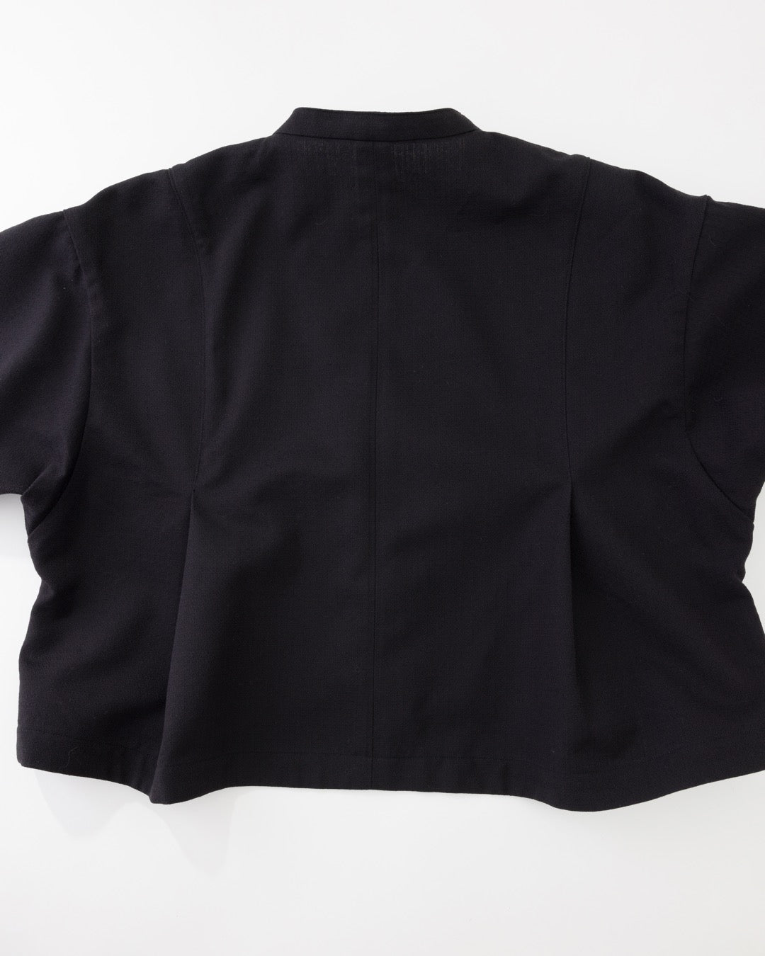 The back view of a black short-sleeve cropped jacket or blazer, laid flat against a white background.