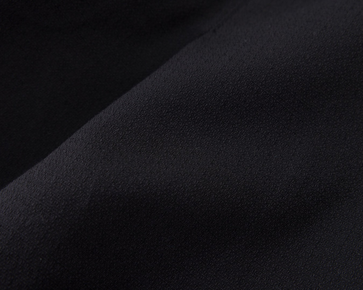 A close-up of a dark fabric surface with soft folds and a matte texture, shown in very dark navy-black tones.