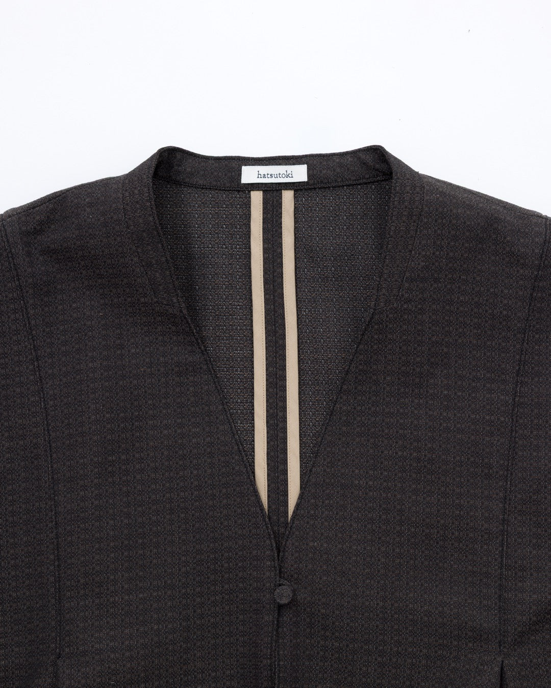 Close-up of a dark textured jacket with a V-neckline, featuring two vertical beige stripes down the centre front and a single button closure.