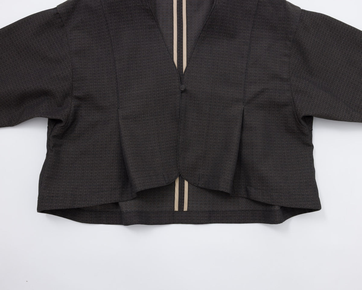 A cropped black textured jacket with long sleeves, a split V-neckline, and two vertical beige stripes running down the centre front, laid flat on a white background.