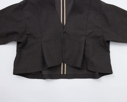 A cropped black textured jacket with long sleeves, a split V-neckline, and two vertical beige stripes running down the centre front, laid flat on a white background.