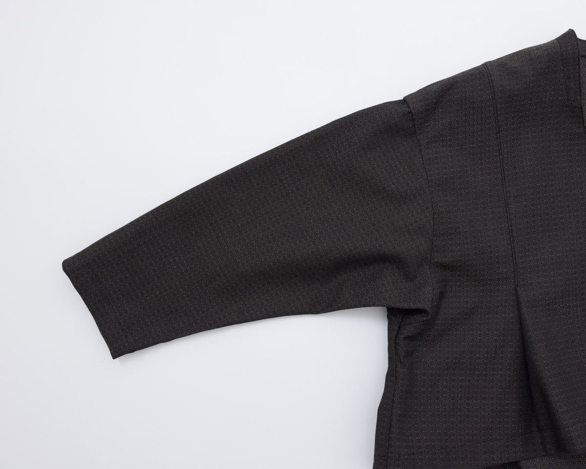 Close-up of a black textured long-sleeve garment laid flat on a white background, showing the sleeve and upper body fabric.