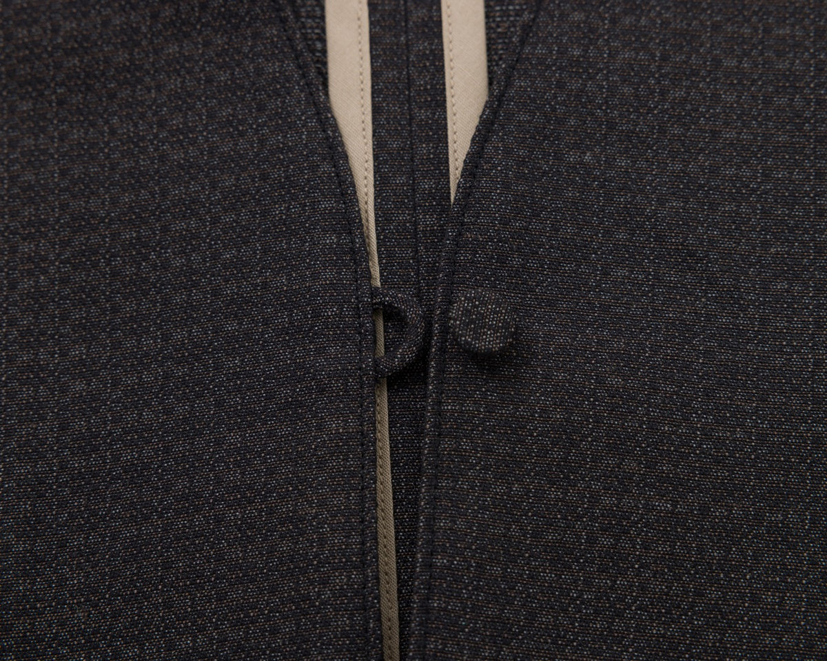 Close-up of a black textured fabric garment with a beige inner lining and a matching dark button closure.