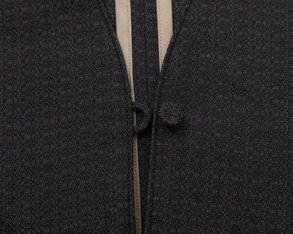 Close-up of a black textured fabric garment with a beige inner lining and a matching dark button closure.