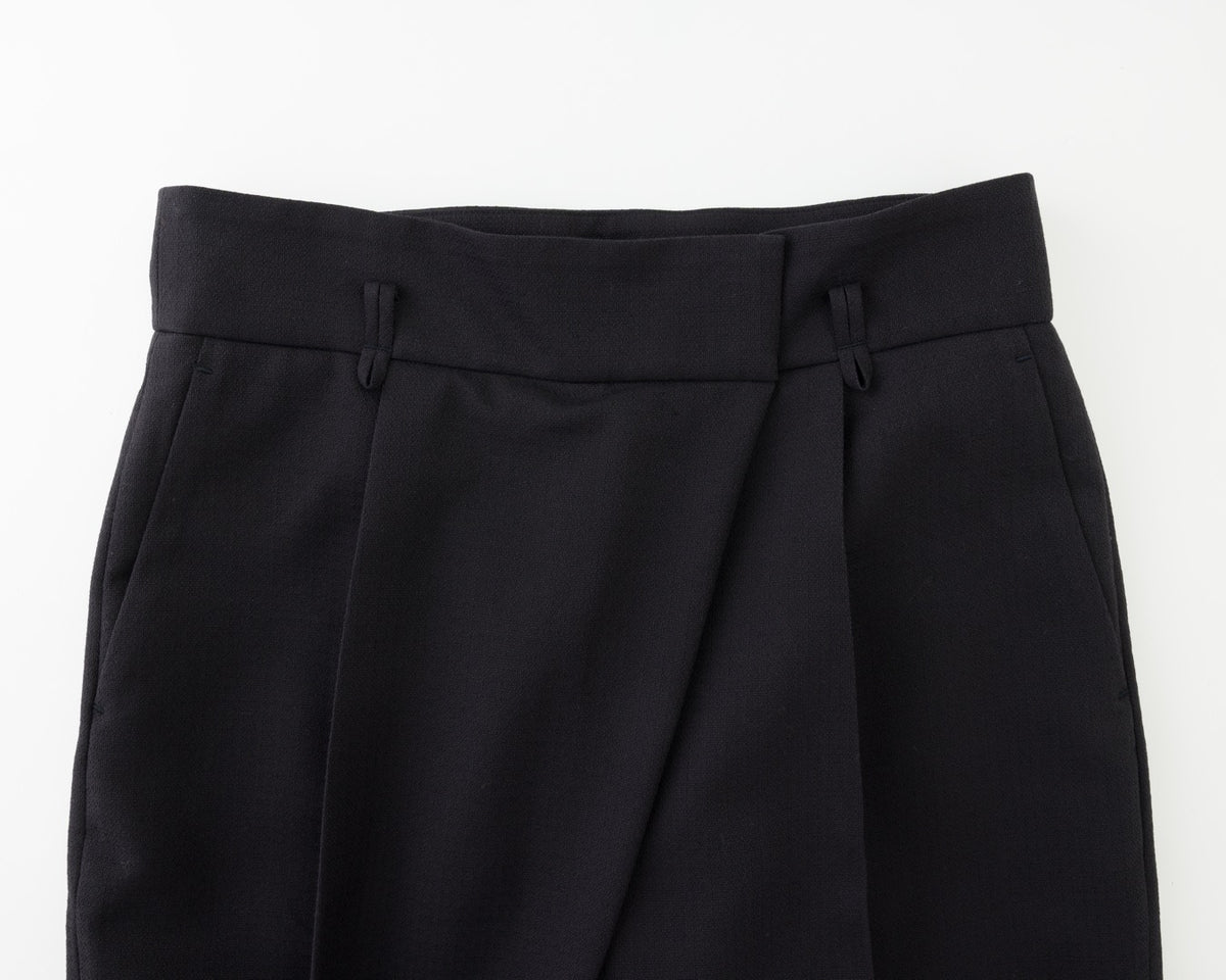 Close-up of black tailored trousers showing the waistband, front pleats, and side pockets against a plain white background.