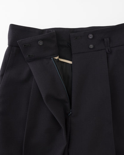 Close-up of black tailored trousers showing the waistband, buttoned flap details, and front closure.