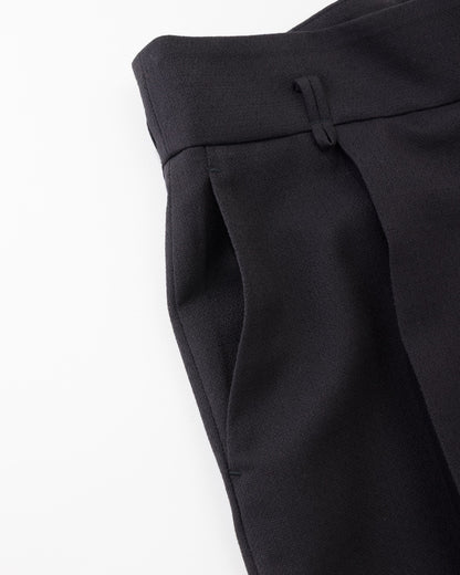 Close-up of black tailored trousers showing the waistband, front pleat, and side pocket on a plain white background.