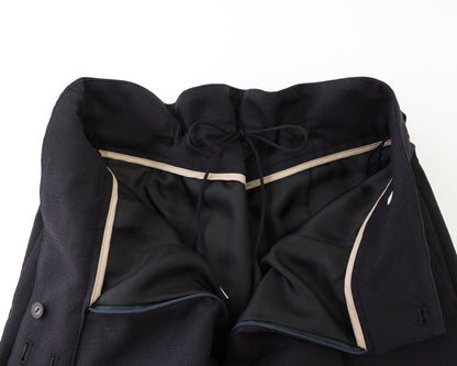 Close-up of a black tailored jacket or coat laid flat on a white background, showing the inner lining, drawstring waistband, and contrast light beige piping.