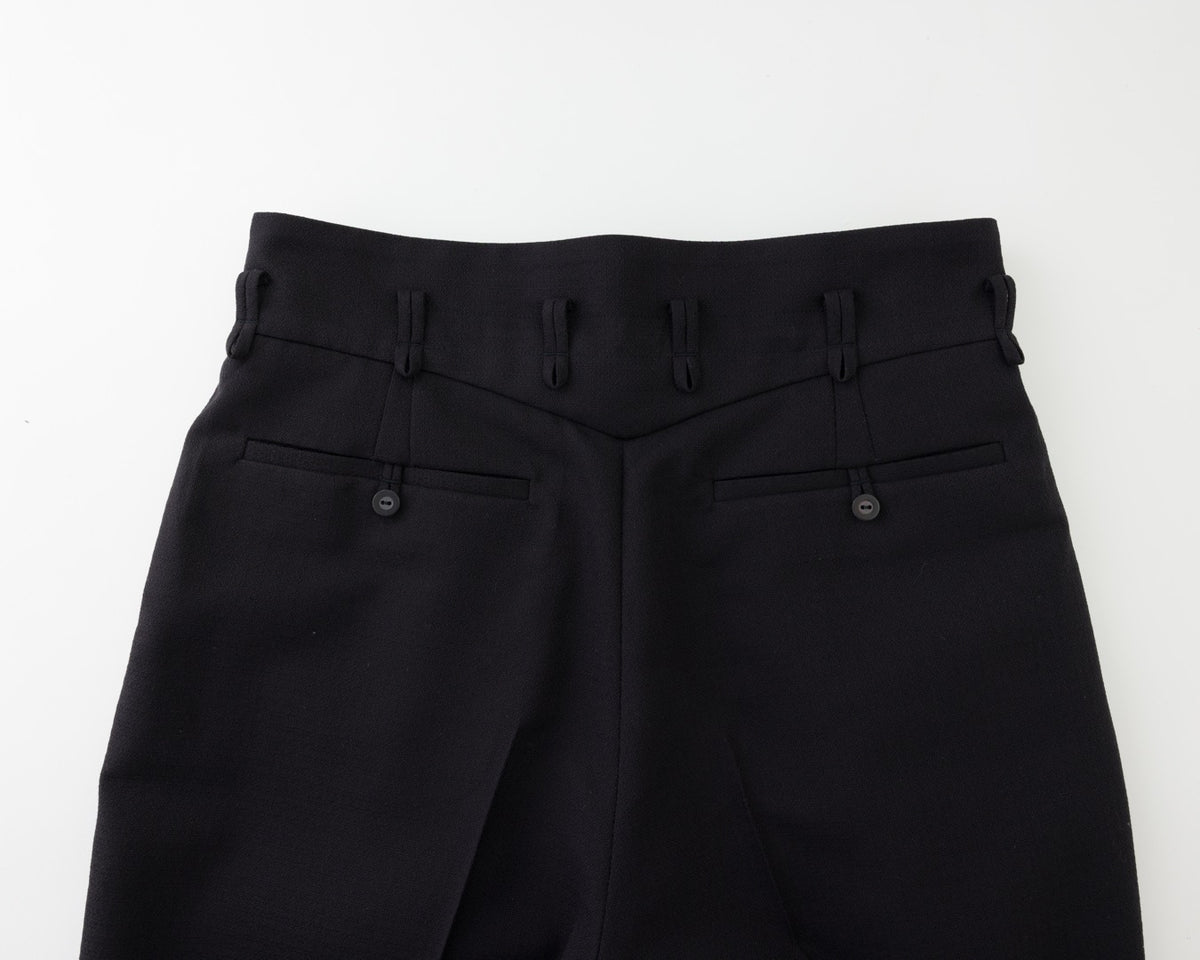 Close-up of the back waistband and rear pockets of black trousers, showing belt loops, button details, and a clean studio background.