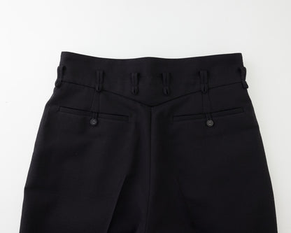 Close-up of the back waistband and rear pockets of black trousers, showing belt loops, button details, and a clean studio background.