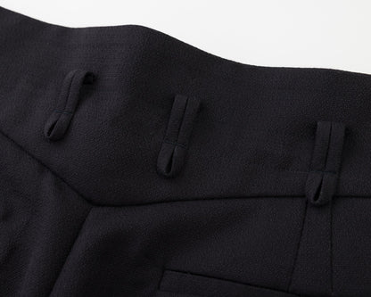 Close-up of a black textured fabric garment, showing pleated details and a pocket on a white background.