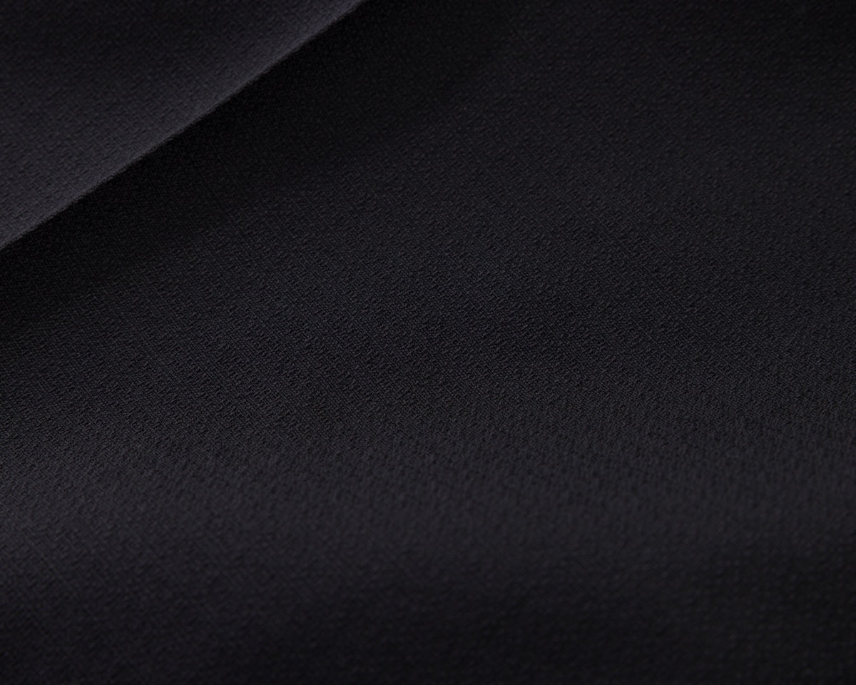 A close-up of a dark solid fabric surface with a soft diagonal fold, showing a very dark navy or near-black textile texture.