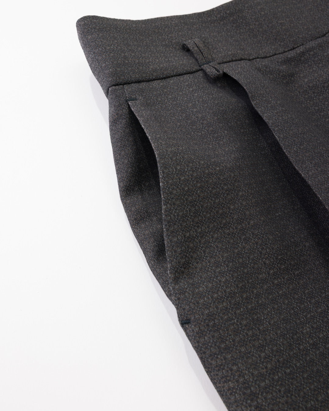 Close-up of black pleated trousers showing the fabric texture and waistband detail against a white background.