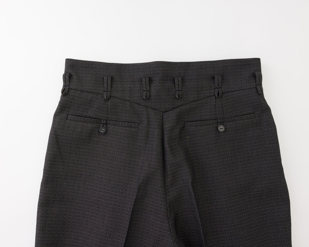 Close-up of the back waistband and rear pockets of black textured trousers, showing belt loops, button details, and fabric weave on a white background.