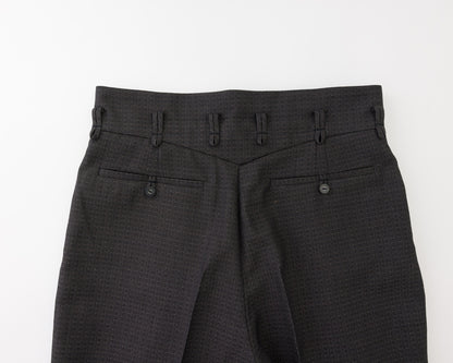 Close-up of the back waistband and rear pockets of black textured trousers, showing belt loops, button details, and fabric weave on a white background.