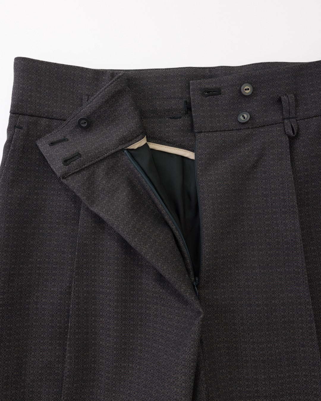 Close-up of black textured wool trousers showing the waistband, button closure, belt loops, and inner waistband lining.