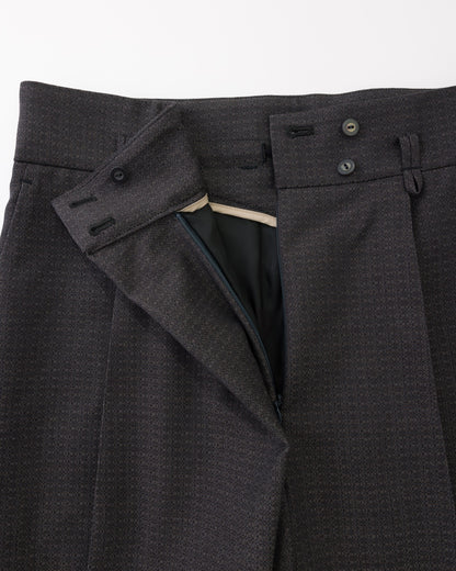 Close-up of black textured wool trousers showing the waistband, button closure, belt loops, and inner waistband lining.