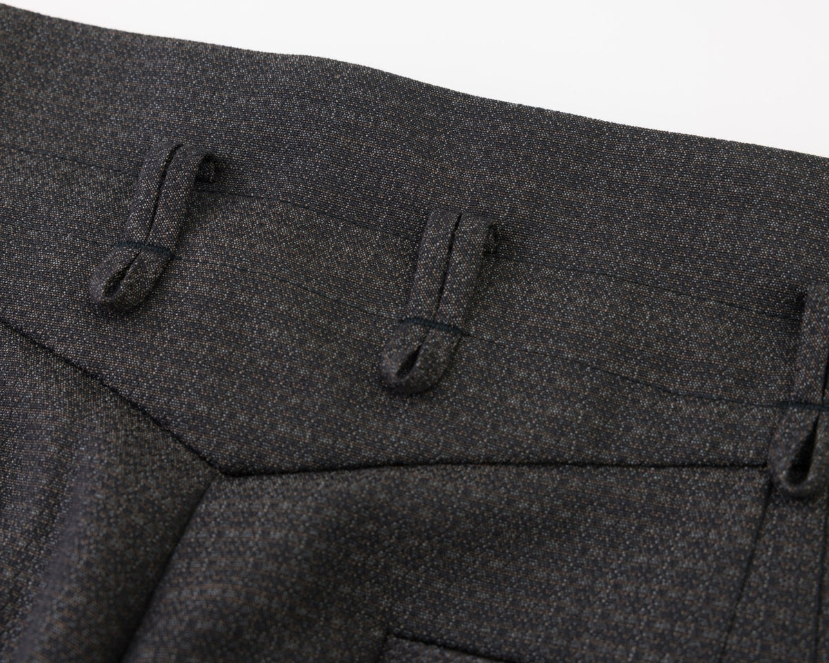 Close-up detail of black textured fabric with belt loops and a pocket on a white background.