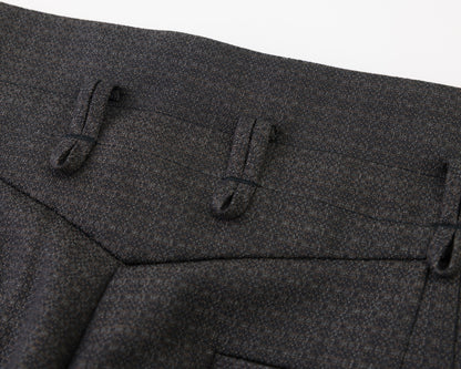 Close-up detail of black textured fabric with belt loops and a pocket on a white background.