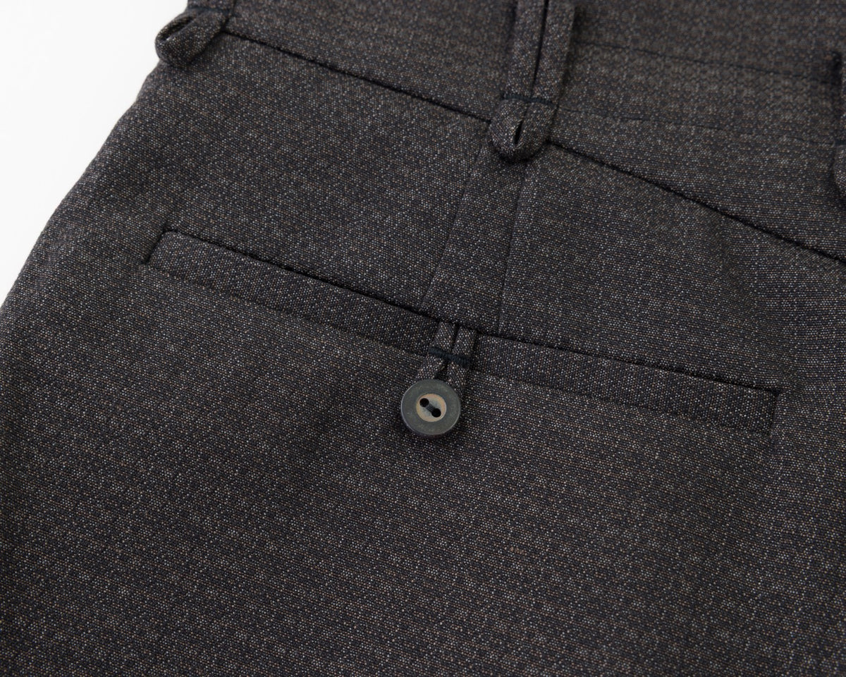 Close-up of black textured fabric showing a buttoned welt pocket and belt loops on trousers.
