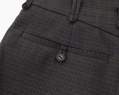 Close-up of black textured fabric showing a buttoned welt pocket and belt loops on trousers.