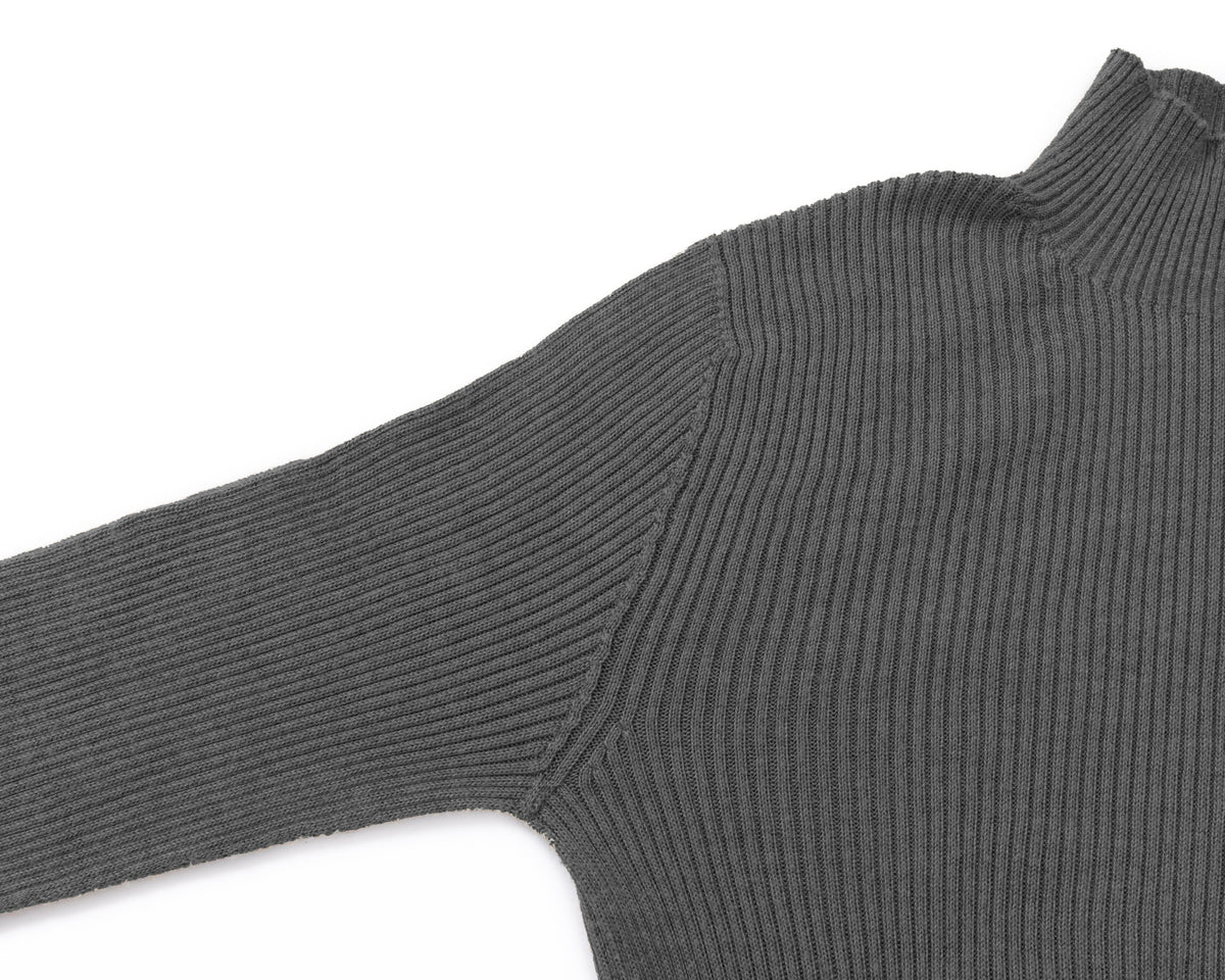 Close-up of a grey ribbed knit turtleneck sweater showing the shoulder seam and sleeve on a white background.