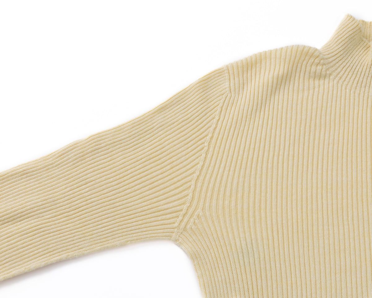 Close-up of a ribbed knit turtleneck sweater in a pale yellow colour, showing the texture and sleeve detail against a plain white background.