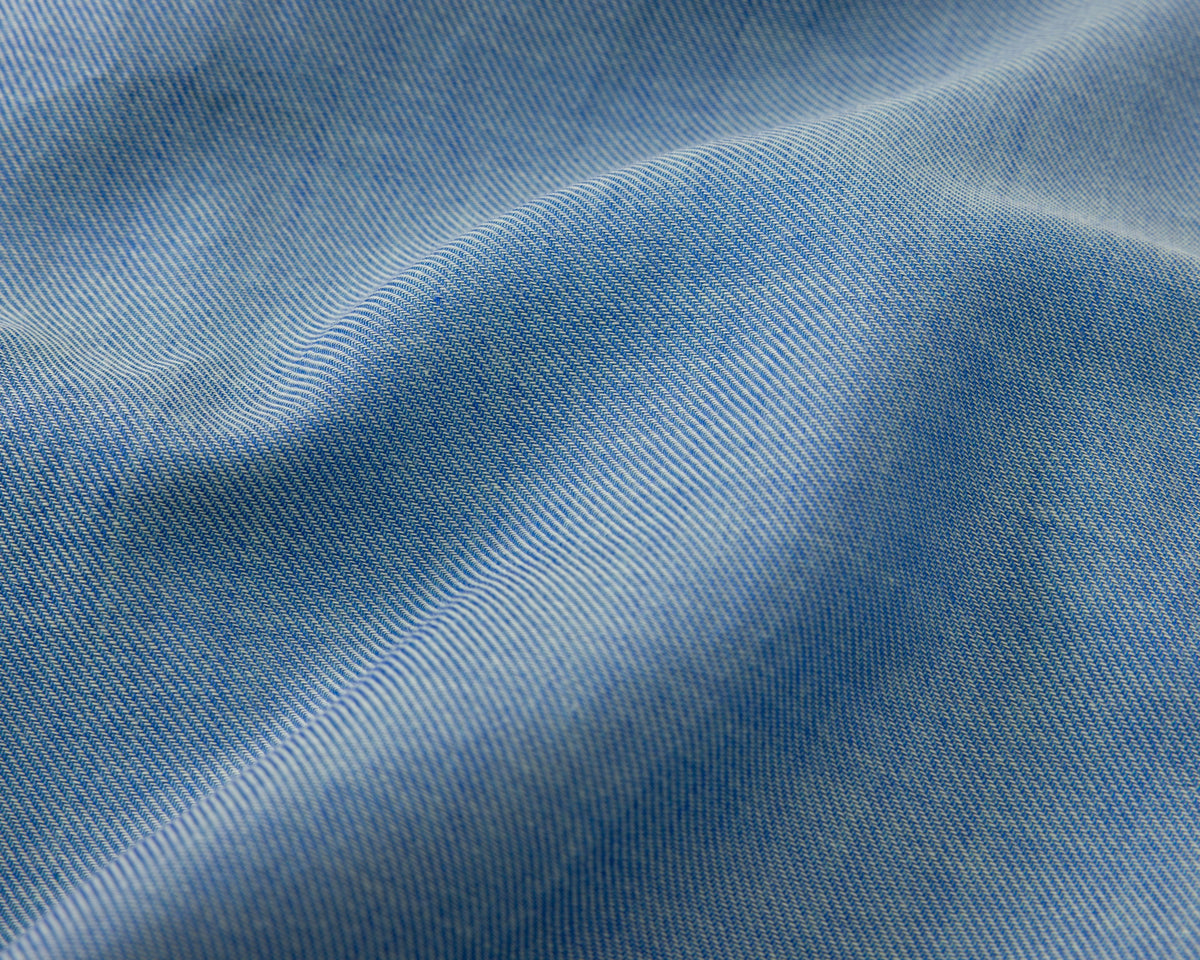 A close-up of light blue fabric with a fine diagonal twill texture and soft folds.