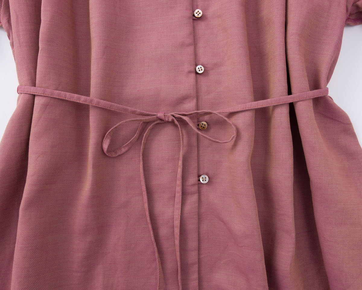 Close-up of a pink shirt with buttons and a tie waist on a white background