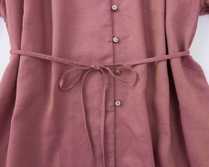 Close-up of a pink shirt with buttons and a tie waist on a white background