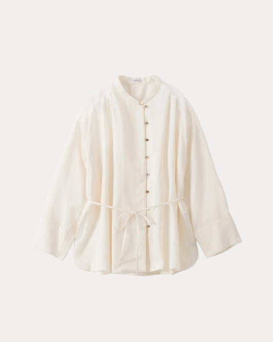 An off-white long-sleeve cotton shirt with a mandarin collar, button-down front, and a drawstring tie at the waist, displayed against a solid off-white background.